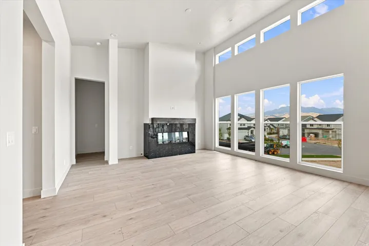 Vaulted ceilings, wood-finish flooring, linear gas fireplace with dark stone surround, multiple tall windows, and transom windows