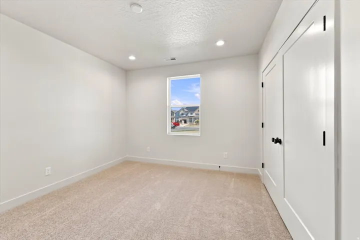 Recessed ceiling lighting, neutral carpet, white walls, and a window with exterior views