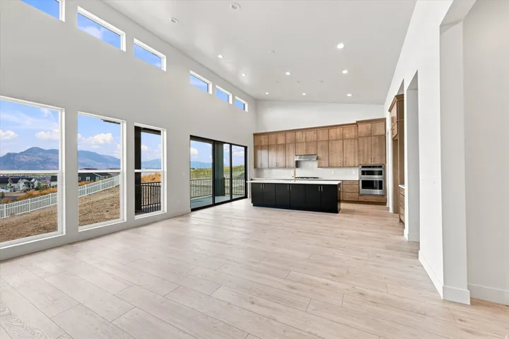 Vaulted ceilings with clerestory windows, light wood-finish flooring, full-height wall of windows, sliding glass door, and a kitchen featuring a dark island with light countertops