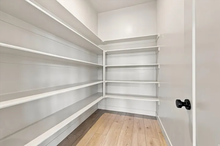 Walk-in pantry with extensive shelving, wood-finish flooring, and a modern black doorknob