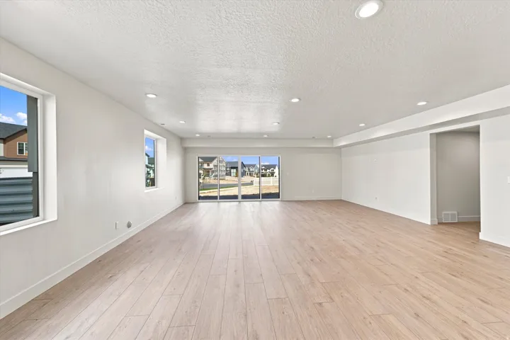 Expansive room featuring light wood-finish flooring, recessed lighting, multiple windows, and sliding glass doors