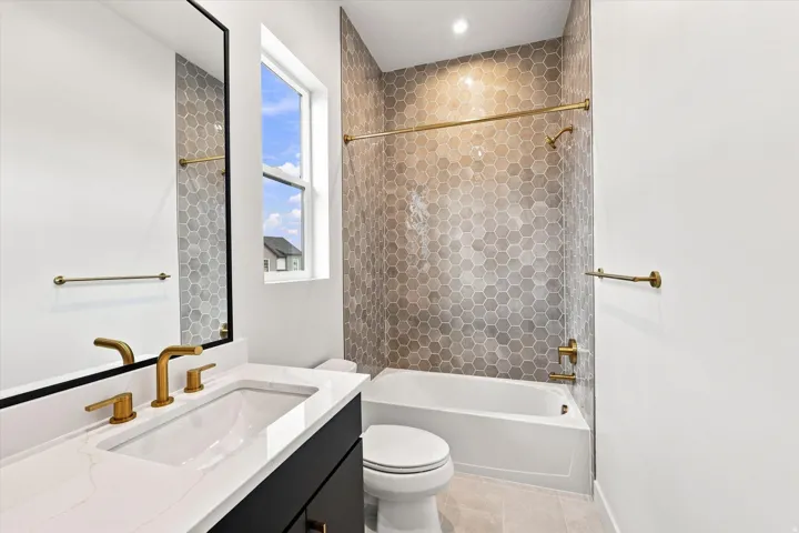 Bathroom featuring a white bathtub, hexagon wall tile, and gold-finish fixtures