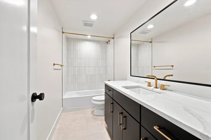 Bathroom featuring a white bathtub with vertical tile surround, a dark wood-finish vanity with a white countertop, and gold-finish fixtures