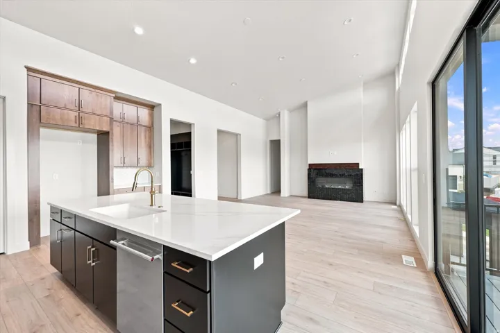 Open-concept living space with light wood-finish flooring, a contemporary fireplace with dark tile surround, and a kitchen island featuring a white countertop and undermount sink