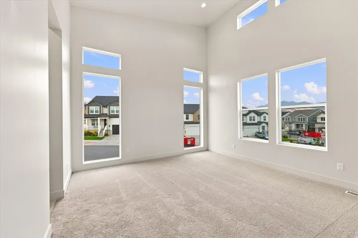 Two-story ceiling, multiple large windows, additional transom windows, light neutral wall paint, and light neutral carpeting