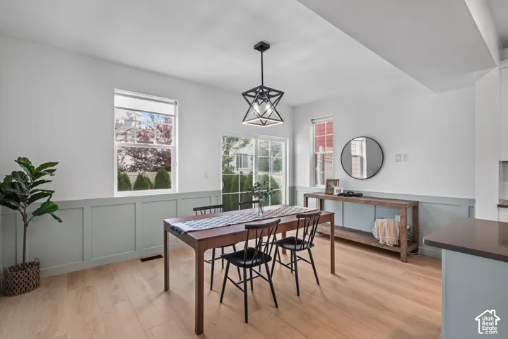 Dining area featuring light wood-finish flooring, white walls with a light green wainscoting, and a contemporary geometric pendant light fixture