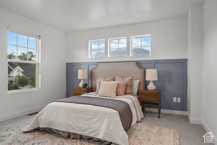 Bedroom featuring a decorative board and batten accent wall, neutral carpeting, and multiple windows providing natural light