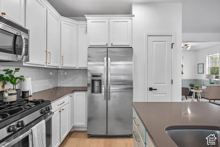 Kitchen featuring white shaker cabinetry, stainless steel appliances, a subway tile backsplash, and light wood-finish flooring
