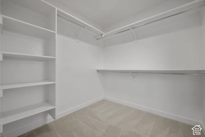 Primary Bedroom Walk-In Closet featuring built-in shelving, two levels of hanging rods, and neutral-toned carpeting