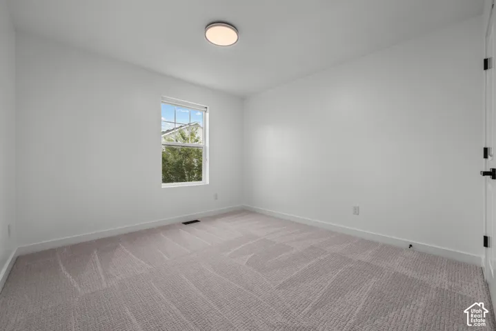 Bright interior space featuring a window with exterior views, light-toned carpet, white baseboards, a flush-mount ceiling light, and a white door with black hardware