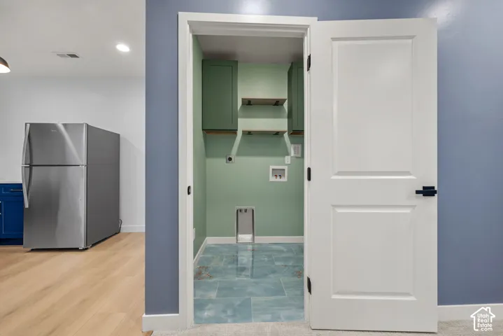 Basement laundry room featuring a tiled floor, sage green walls, and upper cabinetry