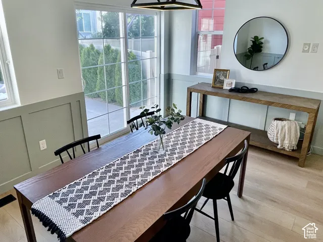 Dining area featuring a contemporary geometric pendant light fixture, wood-finish flooring, sliding glass door, and wainscoting