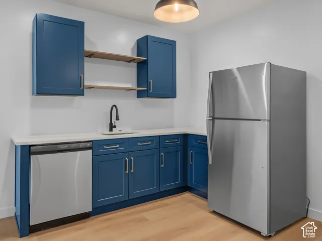 Compact kitchen area featuring blue shaker-style cabinetry, a stainless steel refrigerator, and a matching dishwasher