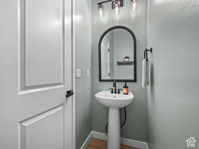 Pedestal sink with matte black faucet, framed by a beaded arch mirror, and illuminated by a three-light vanity fixture