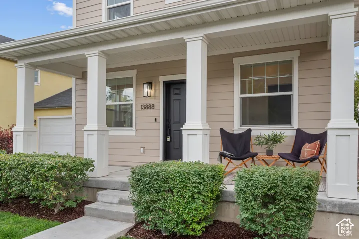 Covered front porch featuring robust white columns, concrete steps, and integrated landscaping with manicured shrubs