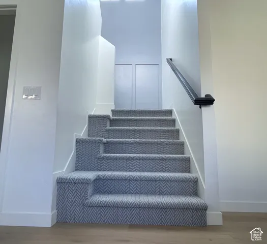Modern staircase featuring gray geometric chevron carpeting, white painted walls, and a black handrail