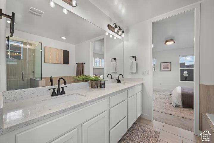 Spacious bathroom featuring a dual vanity with quartz countertops and undermount sinks, matte black fixtures, a large mirror, and a glass-enclosed shower with tiled walls