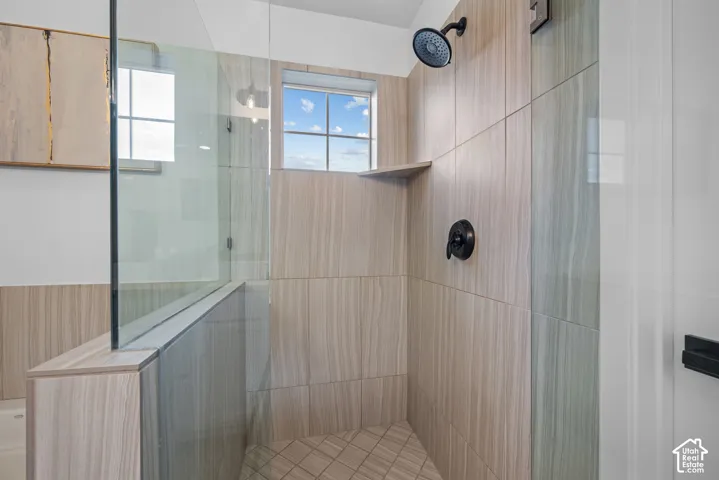 Glass-enclosed shower with full-height wall tiling, integrated shelving, and matte black fixtures