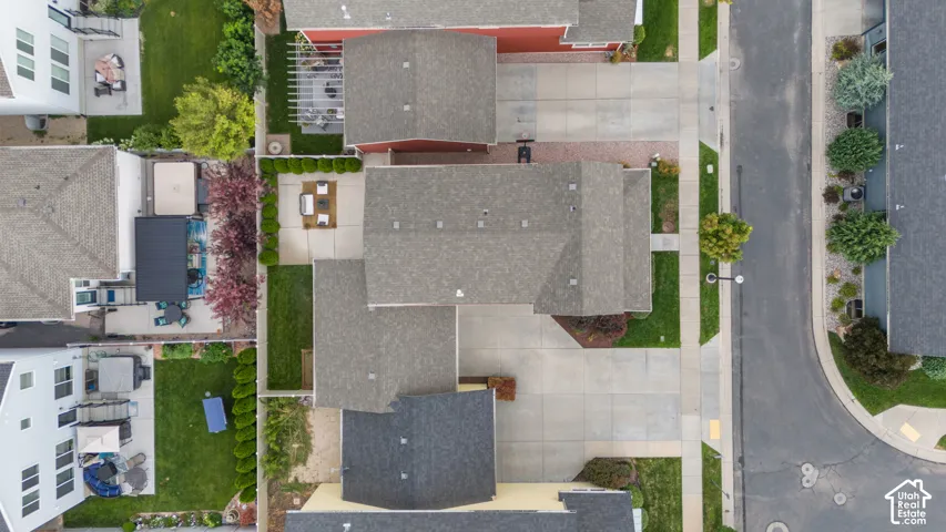 Aerial perspective showcasing a property with a gray shingle roof, a paved driveway, and a concrete patio bordered by manicured shrubs