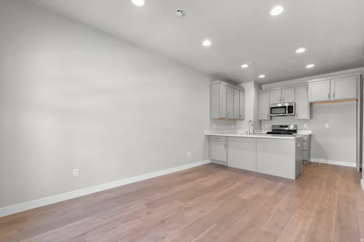 Open-concept living area with wood-finish flooring, a kitchen island, stainless steel microwave, and gas range