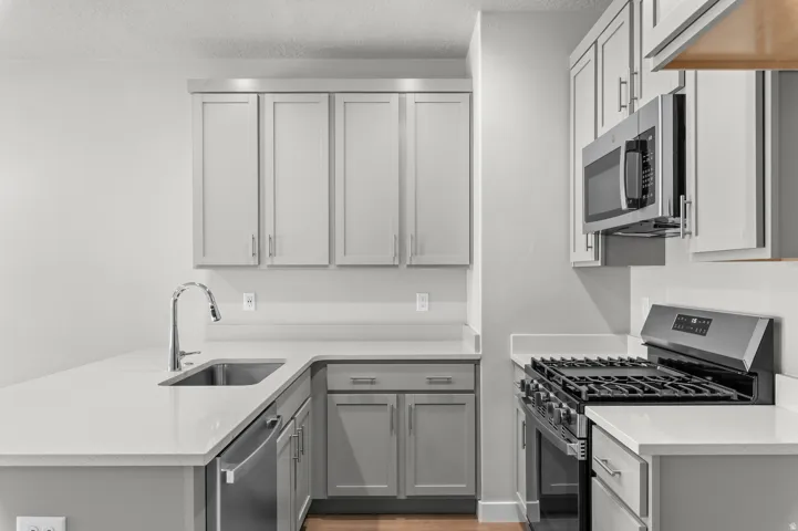 Modern kitchen featuring light gray cabinetry, stainless steel appliances, a gas range, a stainless steel sink, and light-toned countertops