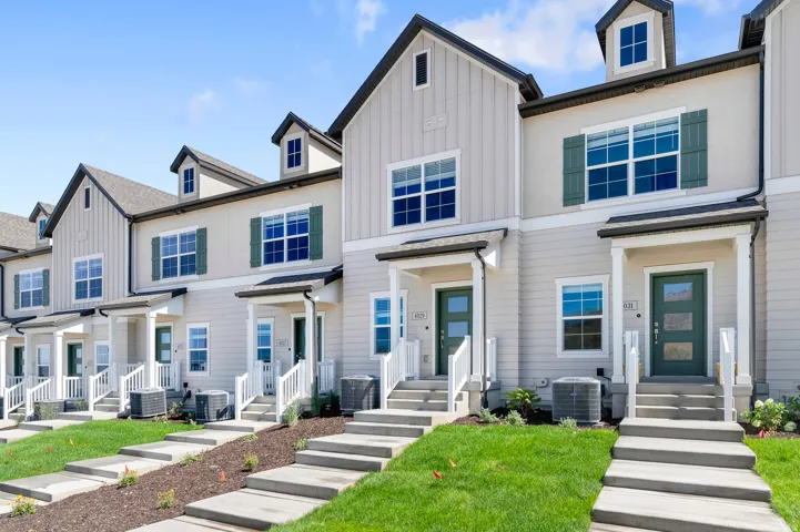 Contemporary townhomes featuring dormer windows, contrasting dark green shutters, columned entryways, and concrete steps leading to each unit