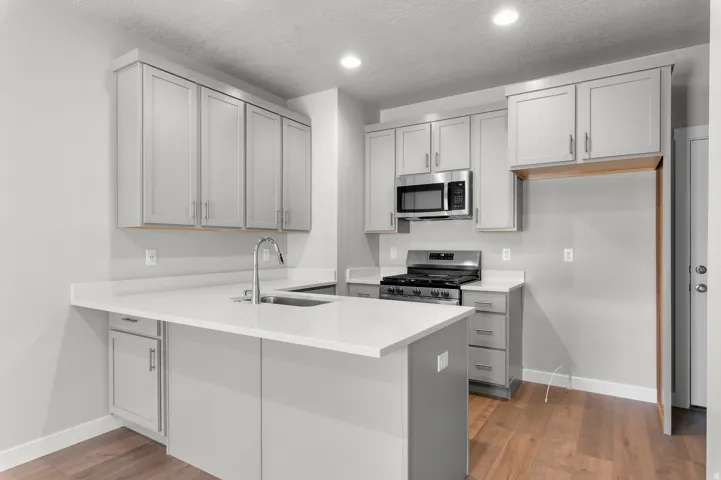 Sleek kitchen featuring light gray cabinetry, white countertops, stainless steel appliances, and wood-finish flooring