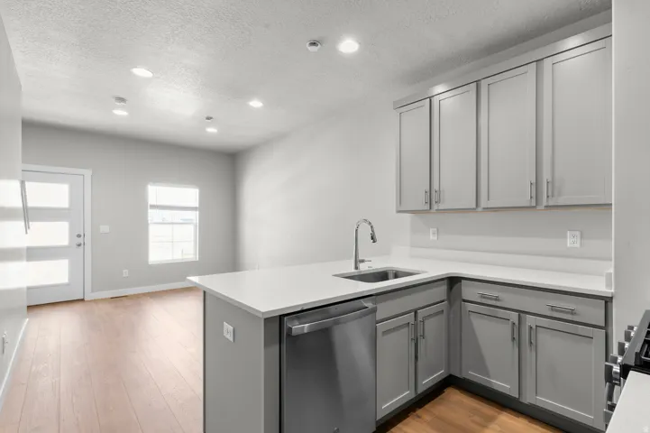 Kitchen featuring gray cabinetry, light-toned countertops, a stainless steel sink with a gooseneck faucet, and integrated stainless steel appliances