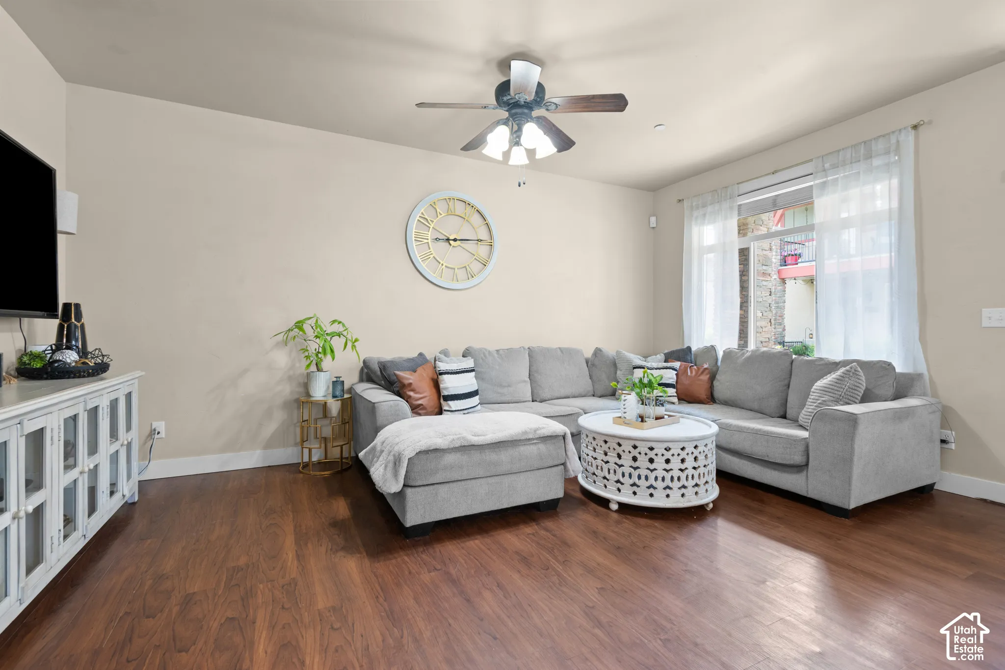 Living area featuring wood-finish flooring, a ceiling fan with light fixture, light-toned walls, and a large window with sheer curtains