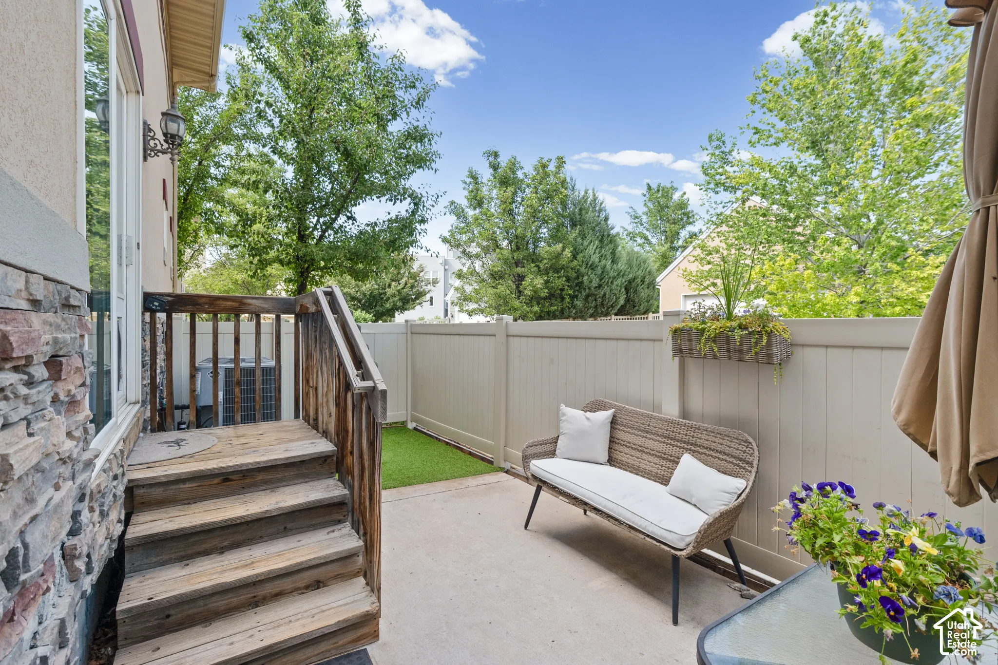 Paved patio area featuring a privacy fence, wood deck with stairs, and a stucco and stone exterior