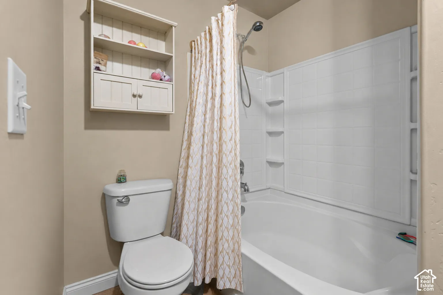 Bathroom featuring a white toilet, built-in wall shelving, and a white bathtub with a tiled shower surround and integrated shelving