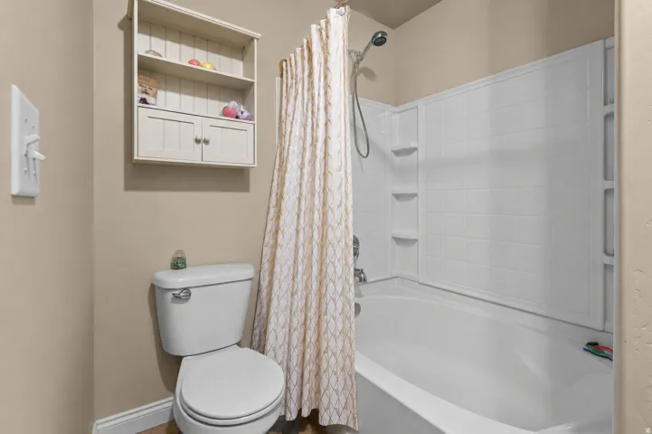 Bathroom featuring a white toilet, built-in wall shelving, and a white bathtub with a tiled shower surround and integrated shelving