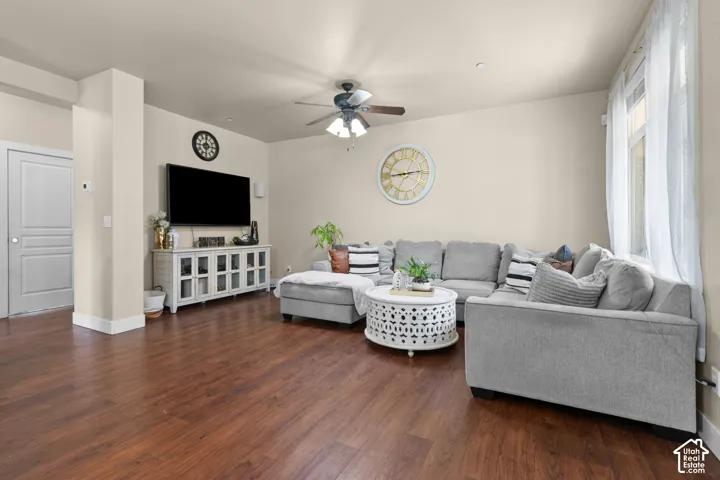 Spacious living area featuring rich wood-finish flooring, a contemporary ceiling fan, and a large window with natural light
