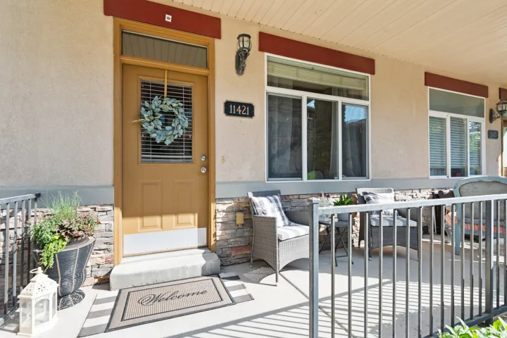 Inviting front entryway featuring a solid-panel door with glass insert, stacked stone wainscoting, stucco exterior, and a covered porch with metal railings