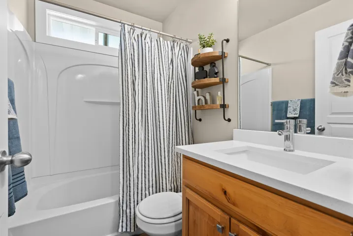 Bathroom featuring a white integrated sink with a single-handle chrome faucet, a wood-finish vanity, and a white fiberglass shower-tub combination