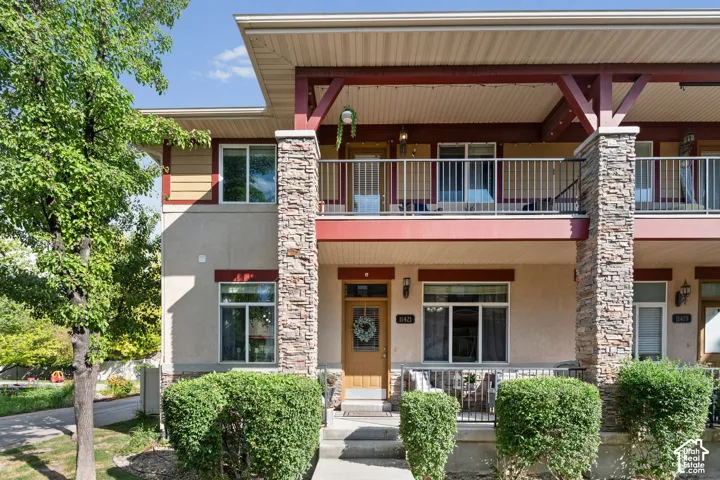 Multi-level townhome featuring a stone-clad facade, a covered front porch, and a second-story balcony with metal railings