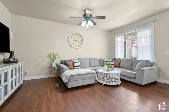 Living area featuring wood-finish flooring, a ceiling fan with light fixture, light-toned walls, and a large window with sheer curtains