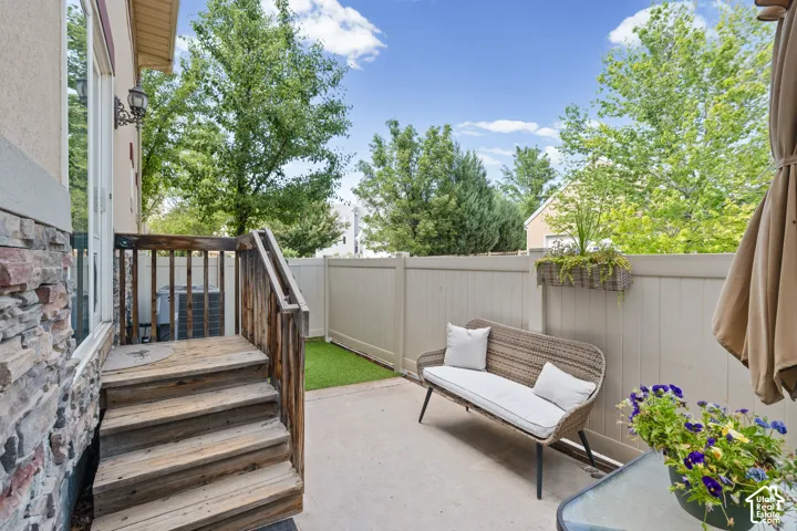 Paved patio area featuring a privacy fence, wood deck with stairs, and a stucco and stone exterior