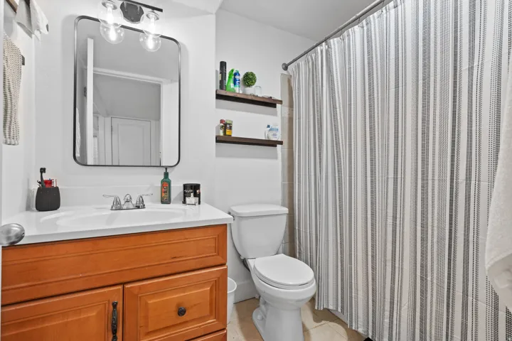 Bathroom featuring a wood-finish vanity with a white countertop and integrated sink, framed mirror, and a chrome light fixture