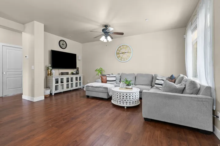 Spacious living area featuring rich wood-finish flooring, a contemporary ceiling fan, and a large window with natural light
