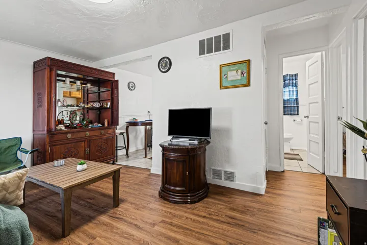 Living area featuring wood-finish flooring, white walls, and a built-in recessed wall register