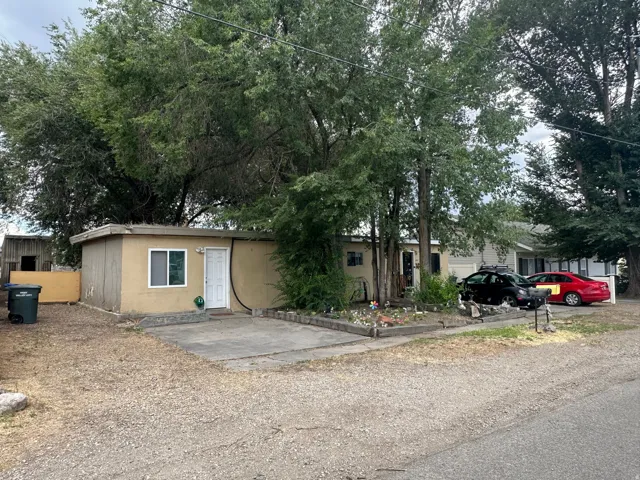 Single-story residence featuring a neutral-toned exterior, mature trees, and a gravel driveway
