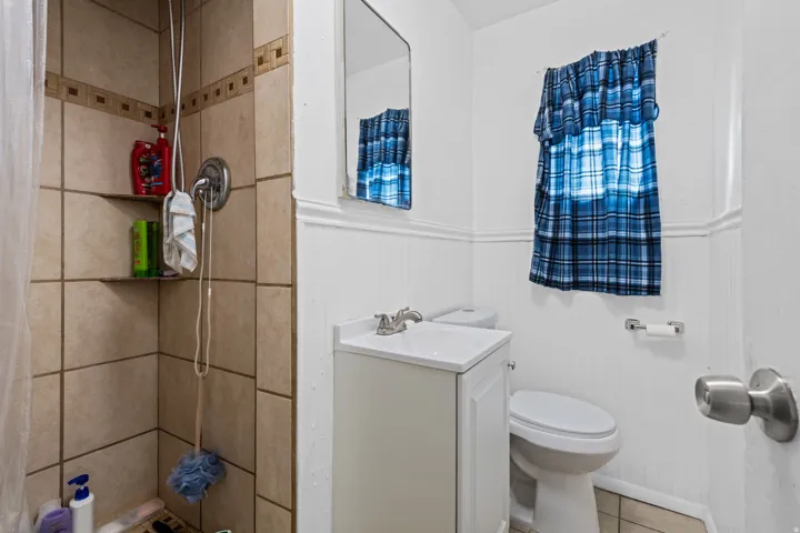 Bathroom featuring a tiled shower with integrated shelving, beadboard wainscoting, and a single vanity with a white countertop
