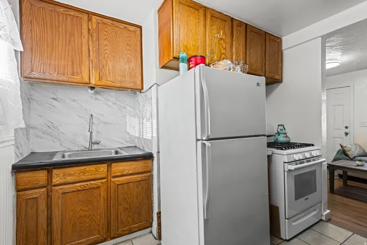 Compact kitchen with wood cabinetry, white marble-patterned backsplash, and dark countertops