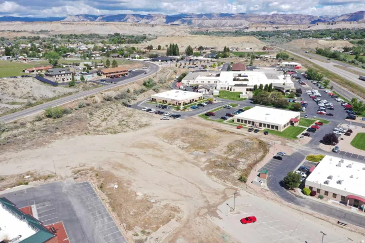 Expansive undeveloped land parcel featuring surrounding commercial buildings, paved roads, and distant mountainous terrain