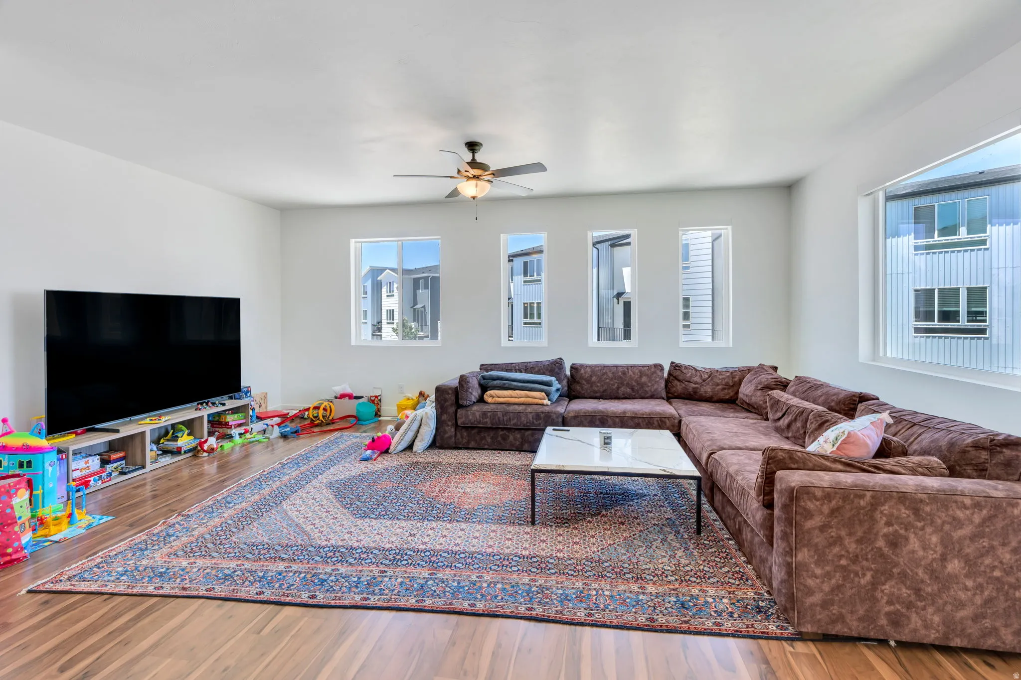 Spacious interior room featuring wood-finish flooring, white walls, and multiple windows