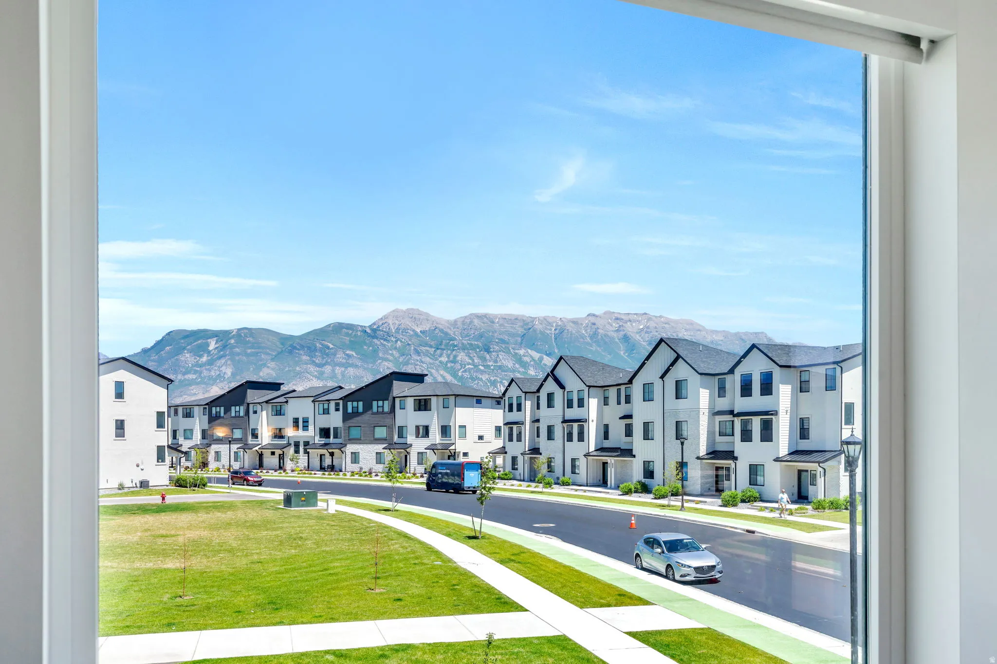 Expansive mountain scenery framing a residential street with contemporary townhomes and a manicured green space