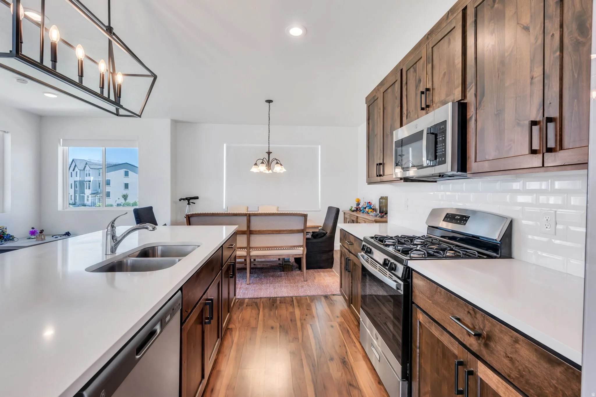 Contemporary kitchen featuring white countertops, stainless steel appliances, wood-finish flooring, dark wood cabinetry, and a subway tile backsplash