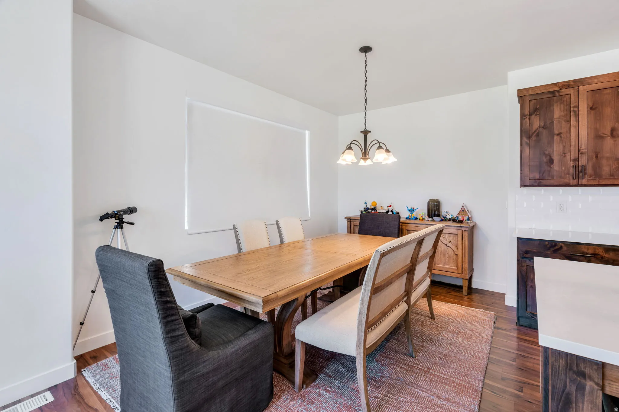 Dining area with wood-finish flooring, white walls, and a window with a roller shade