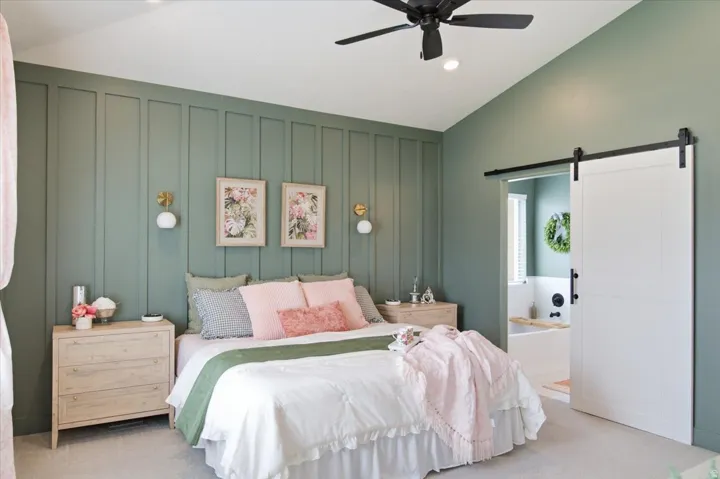 Bedroom featuring an accent wall with vertical paneling, vaulted ceiling, and a ceiling fan